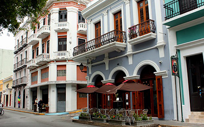 Una calle con edificios de estilo colonial con balcones y un café en frente de uno de los edificios.